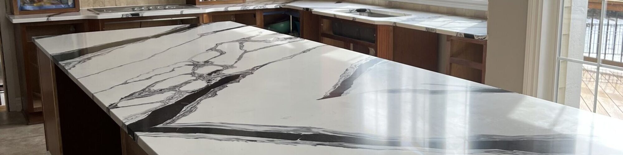 A long kitchen island in veined white and grey stone, the veining running unbroken along its full length and into the counter beyond